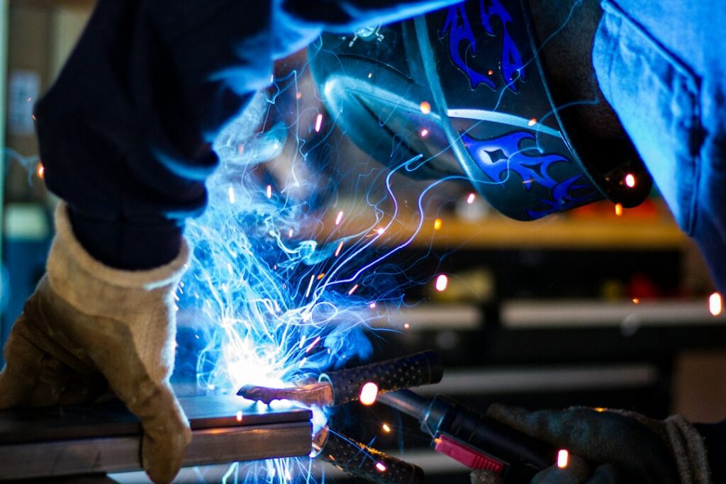 Welder wearing a protective helmet and gloves welding a metal assembly